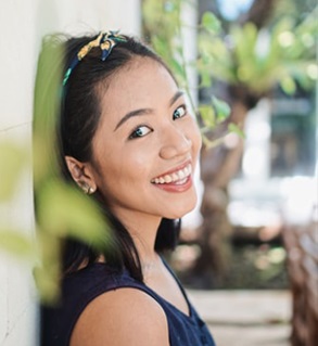 壁にもたれながら笑顔を見せるアジア人女性の写真
